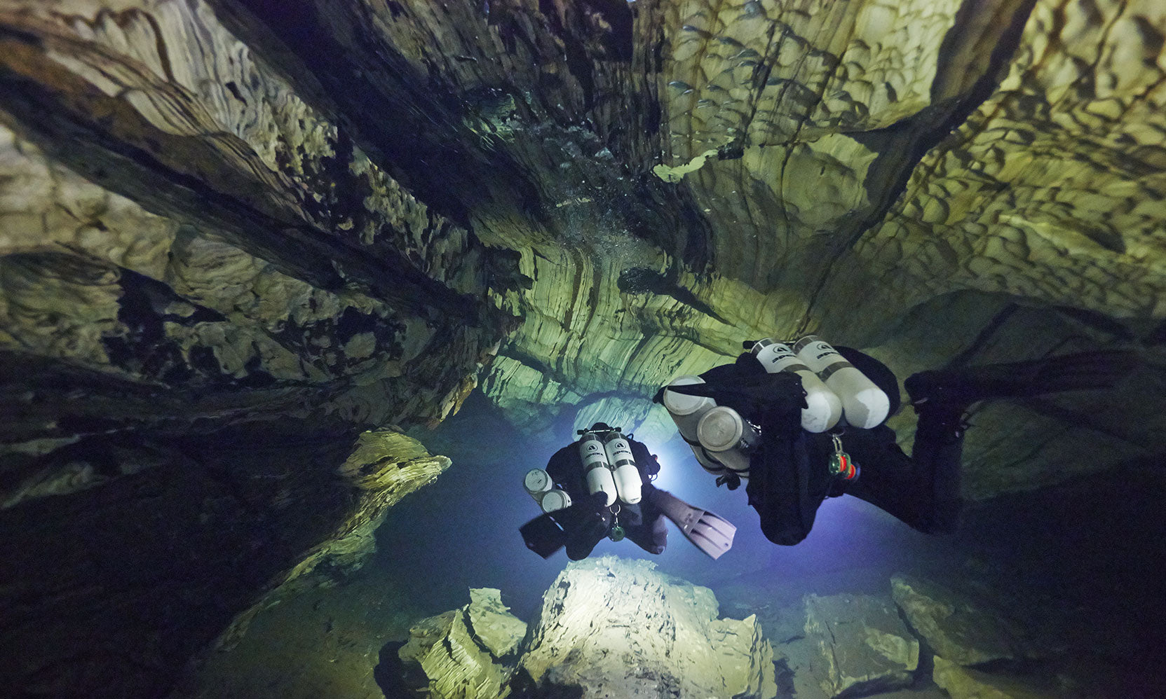 Divers in black wetsuits exploring an underwater cave